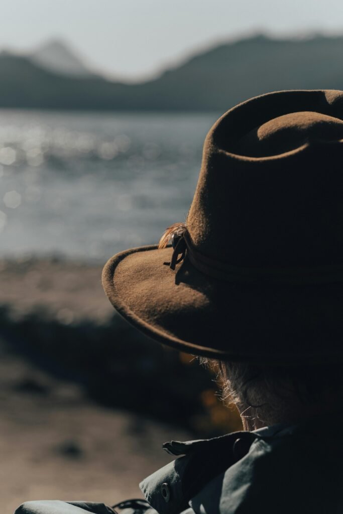 Rear view of a person wearing a brown fedora hat, looking at a tranquil ocean scene.